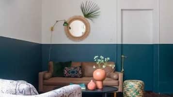 A room with a patterned chair, a sofa with cushions, a round mirror, and a door.