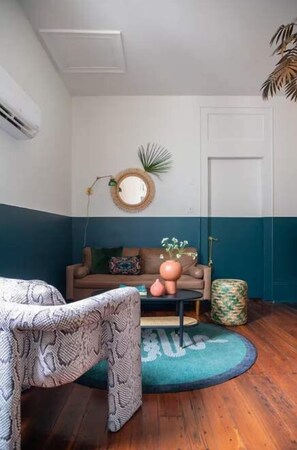 A room with a patterned chair, a sofa with cushions, a round mirror, and a door. - Prime Uptown location - Designer 1BD w outdoors! (New Orleans)