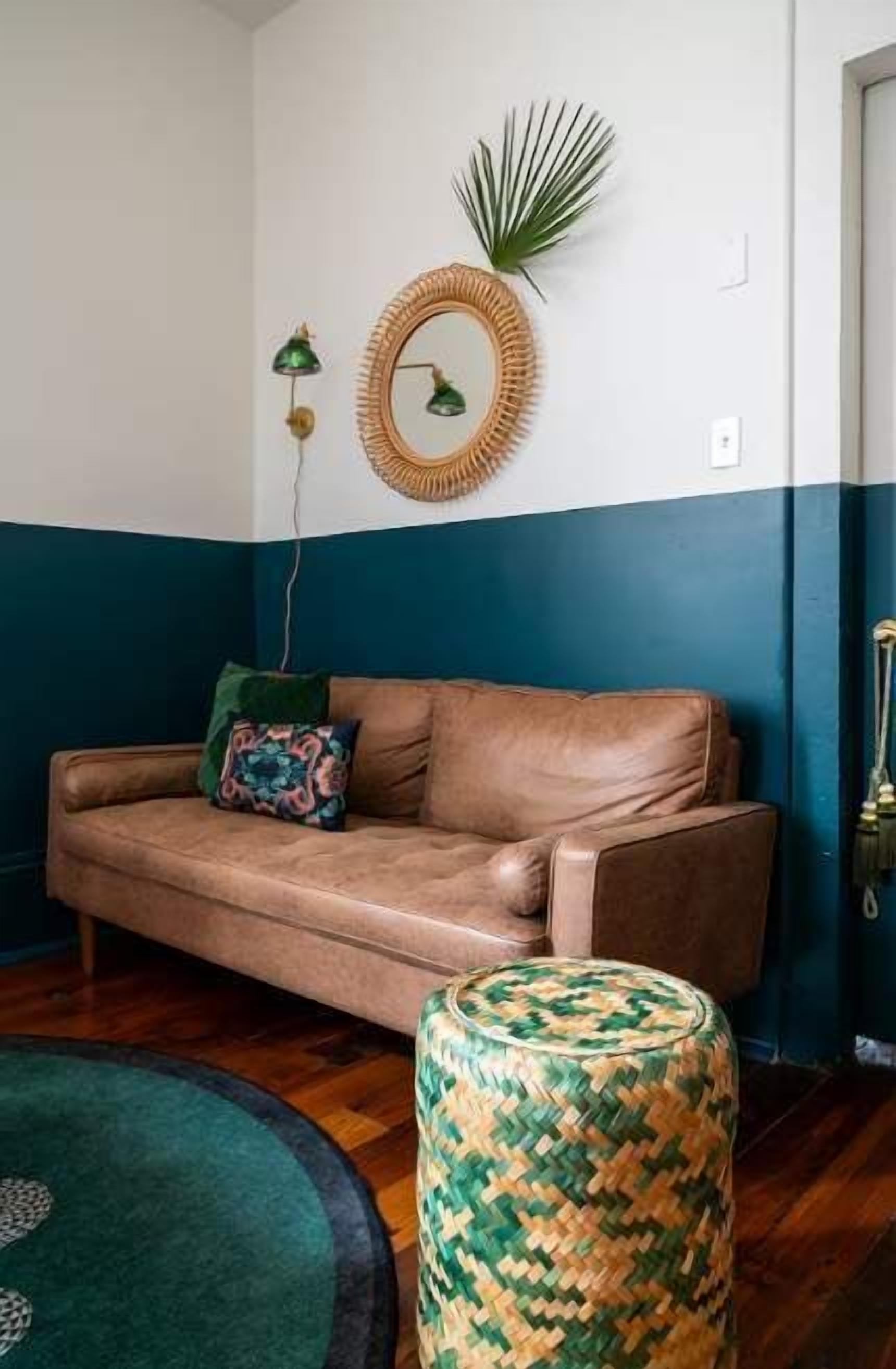 A room with a brown leather sofa, a woven stool, and a round mirror on the wall.