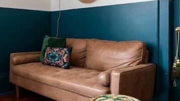 A room with a brown leather sofa, a woven stool, and a round mirror on the wall.