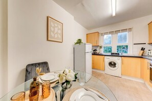 Eine kompakte Küche mit Waschmaschine, Kühlschrank und Essbereich mit Tisch für zwei Personen.