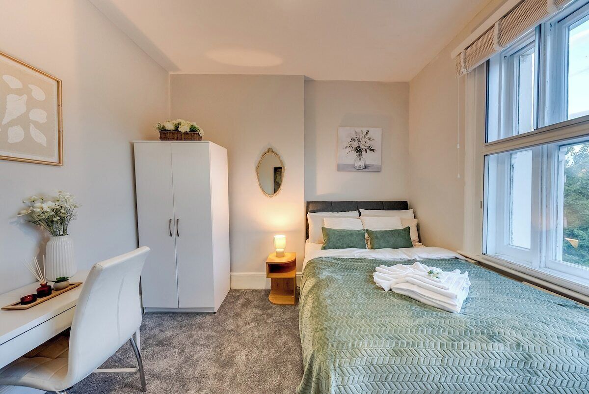 A bedroom with a bed, a desk, a wardrobe, a mirror, and a window.
