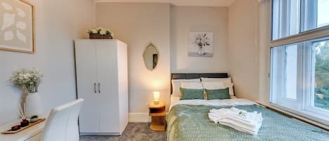 A bedroom with a bed, a desk, a wardrobe, a mirror, and a window.