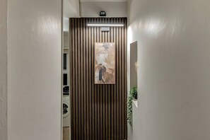 Ein Flur mit einer Holzwand, einem gerahmten abstrakten Gemälde, einer Wandleuchte und einem Blumentopf.