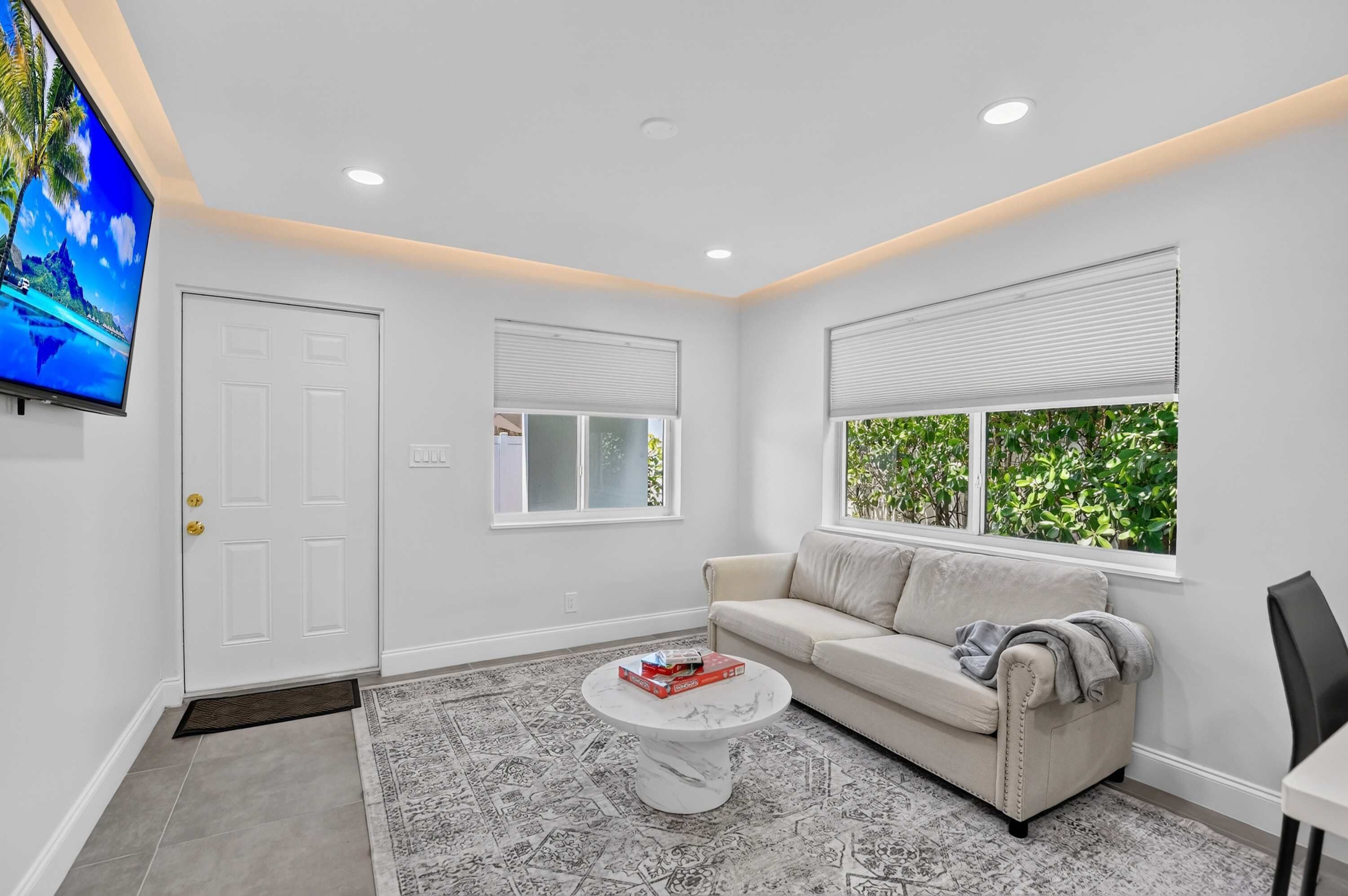 A modern living room with a sofa, a coffee table, a television, and a window with blinds.
