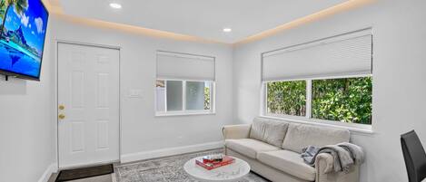 A modern living room with a sofa, a coffee table, a television, and a window with blinds.