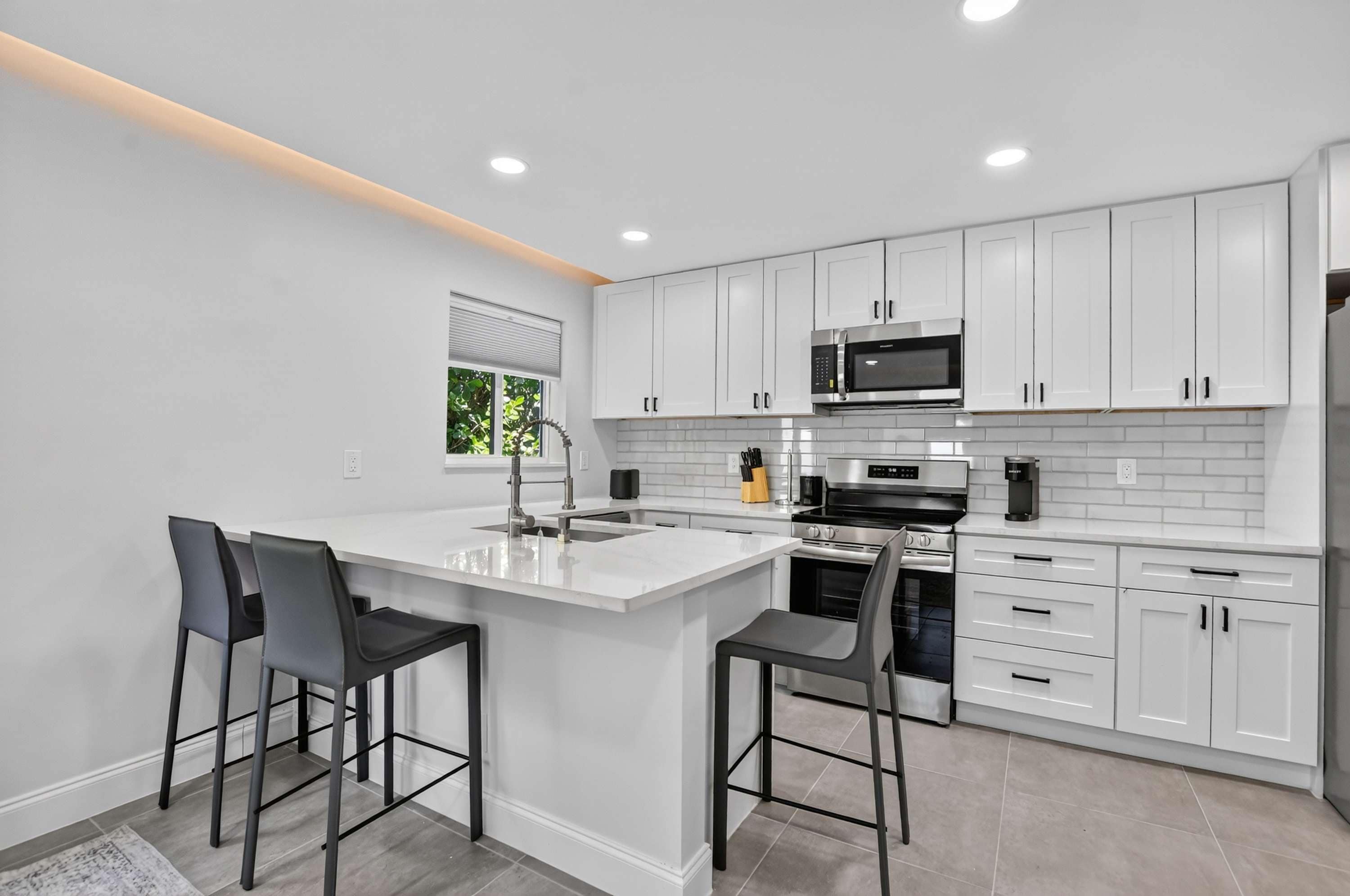 A modern kitchen with white cabinets, stainless steel appliances, and a central island with bar stools.