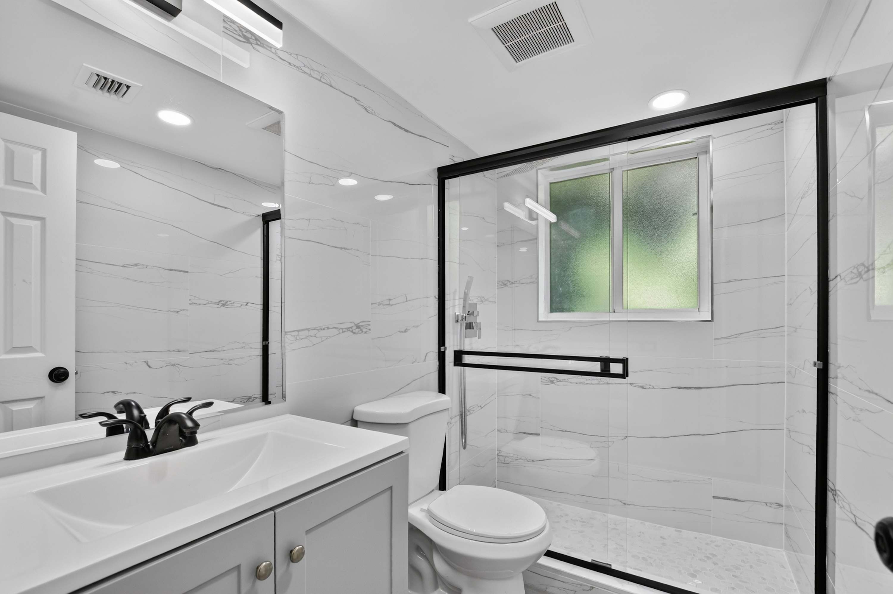 Een moderne badkamer met een wastafel van wit marmer, een toilet en een douchecabine met glazen wanden.
