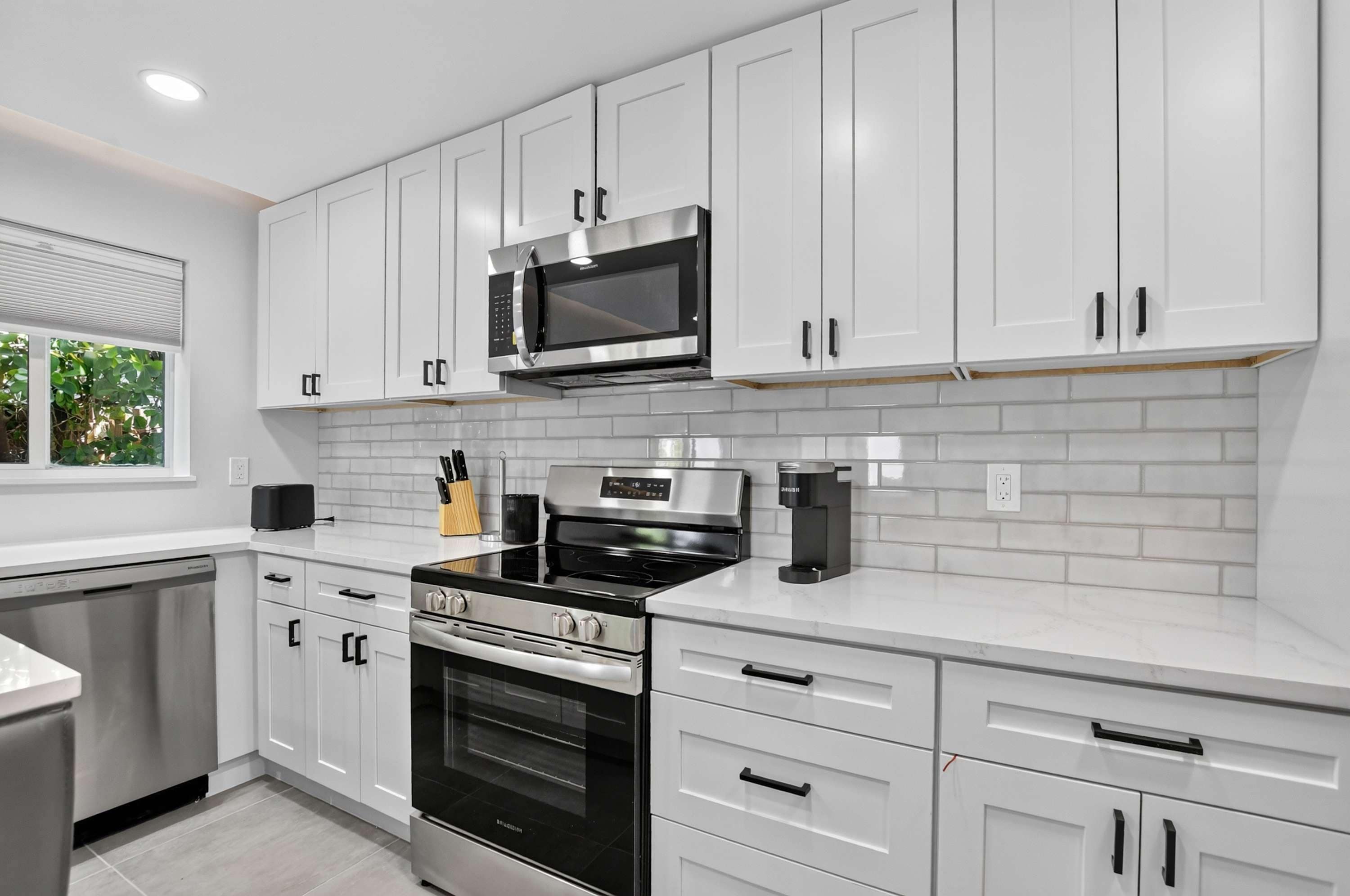 Una cocina moderna con armarios blancos, un microondas de acero inoxidable, una estufa a gas y un horno empotrado.