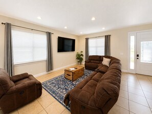 A living room with a sectional sofa, two armchairs, a coffee table, and a flat-screen TV on the wall. - Reunion Resort 6BR Pool Home & Game Room (Kissimmee)