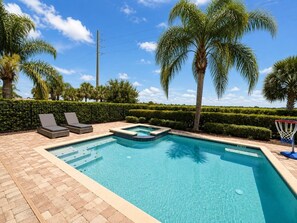 Una piscina con due lettini, un canestro da basket e palme.