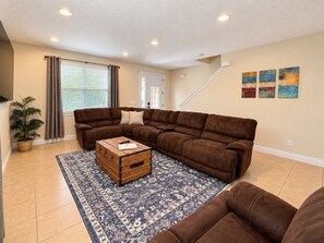 A living room with a sectional sofa, a wooden chest, and a patterned rug. - Reunion Resort 6BR Pool Home & Game Room (Kissimmee)