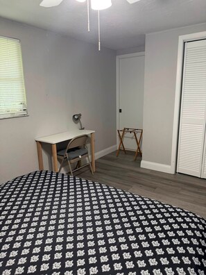 Ein Schlafzimmer mit Bett, Schreibtisch, Stuhl, Pendelleuchte und Kleiderschrank.