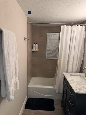 Ein Badezimmer mit einer Badewanne, einer Dusche, einem weißen Handtuch und Ablage für Toilettenartikel.