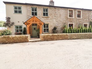 A stone building with a wooden entrance, a stone wall, and a gravel driveway. - Cottage by the River (Burnley)