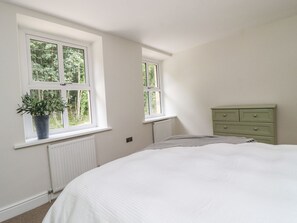 A bedroom with a bed, two windows, a radiator, and a dresser. - Cottage by the River (Burnley)