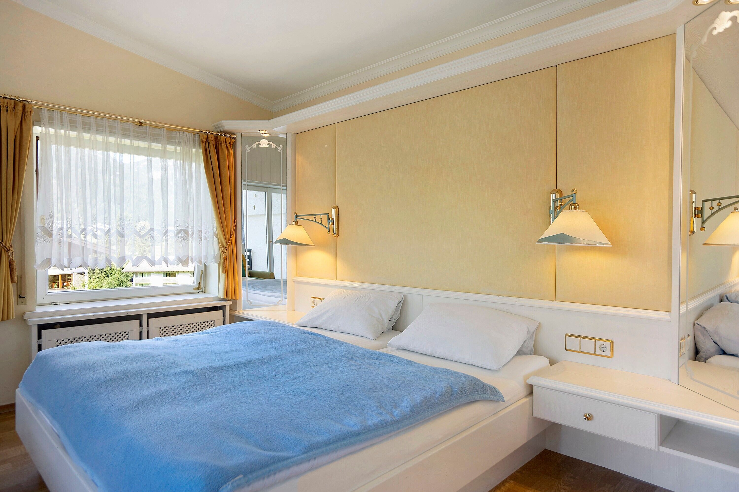 Ein Hotelzimmer mit Bett, Nachttischen, einem Fenster mit Vorhängen und Wandlampen.