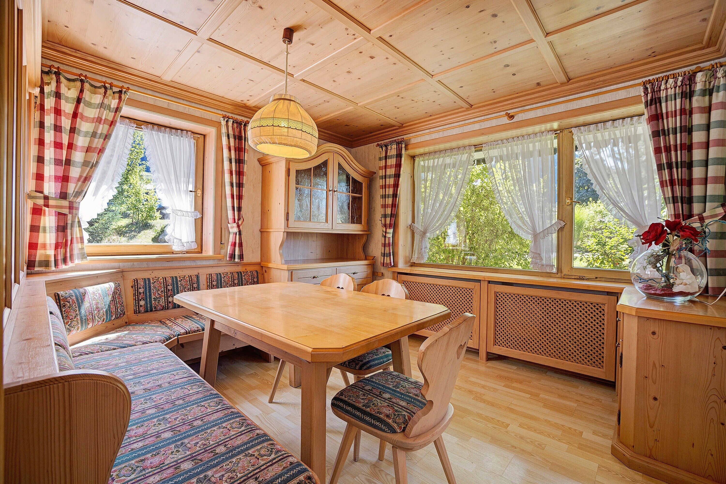 L’intérieur d’un chalet en bois, avec une table à manger, des bancs et une grande fenêtre agrémentée de rideaux.