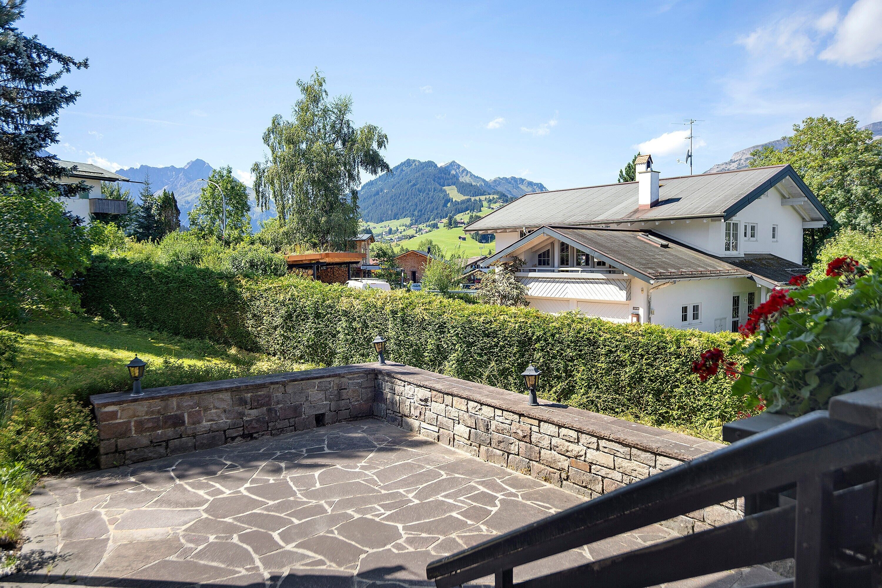 A stone patio with a stone wall, a wooden fence, and a view of a house with a mountain backdrop.