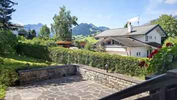 A stone patio with a stone wall, a wooden fence, and a view of a house with a mountain backdrop.