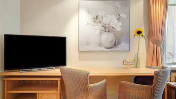 A room with a television on a wooden stand, a painting of flowers on the wall, and two wicker chairs.