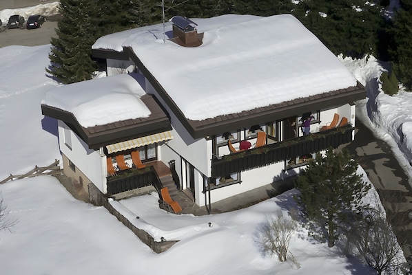 A snow-covered two-story house with a balcony and a covered porch.