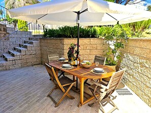 Eine Terrasse im Freien mit einem runden Holztisch, Stühlen und einem großen Sonnenschirm.