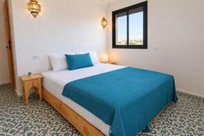 Un dormitorio con cama, mesita de noche, ventana y suelo con baldosas estampadas.