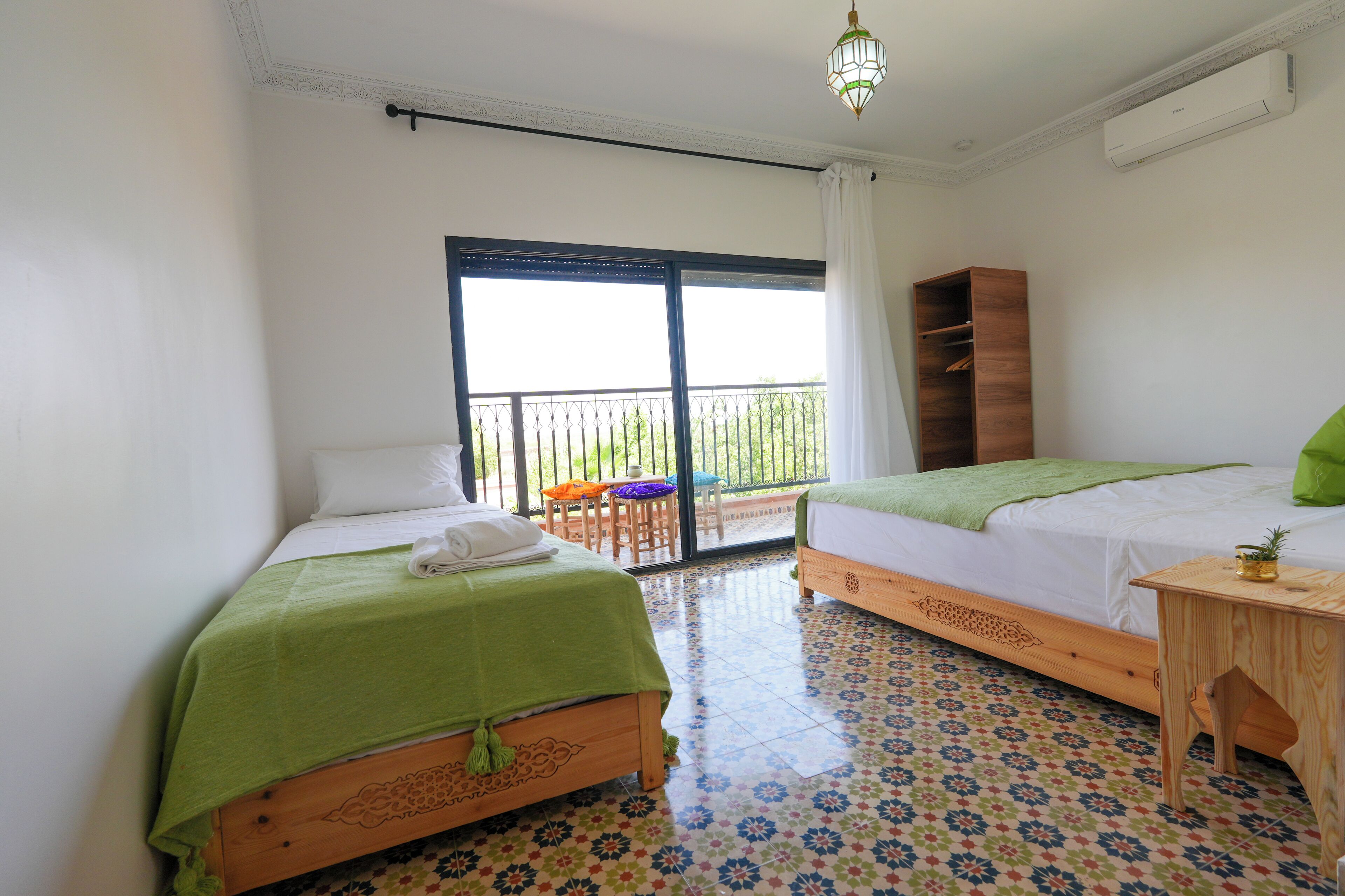 A hotel room with two beds, a balcony, a wooden nightstand, and a patterned floor.