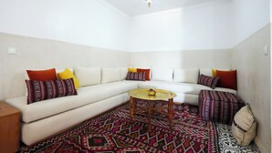 Una sala de estar con un sofá blanco, cojines estampados, una mesa de centro redonda y una alfombra tradicional.