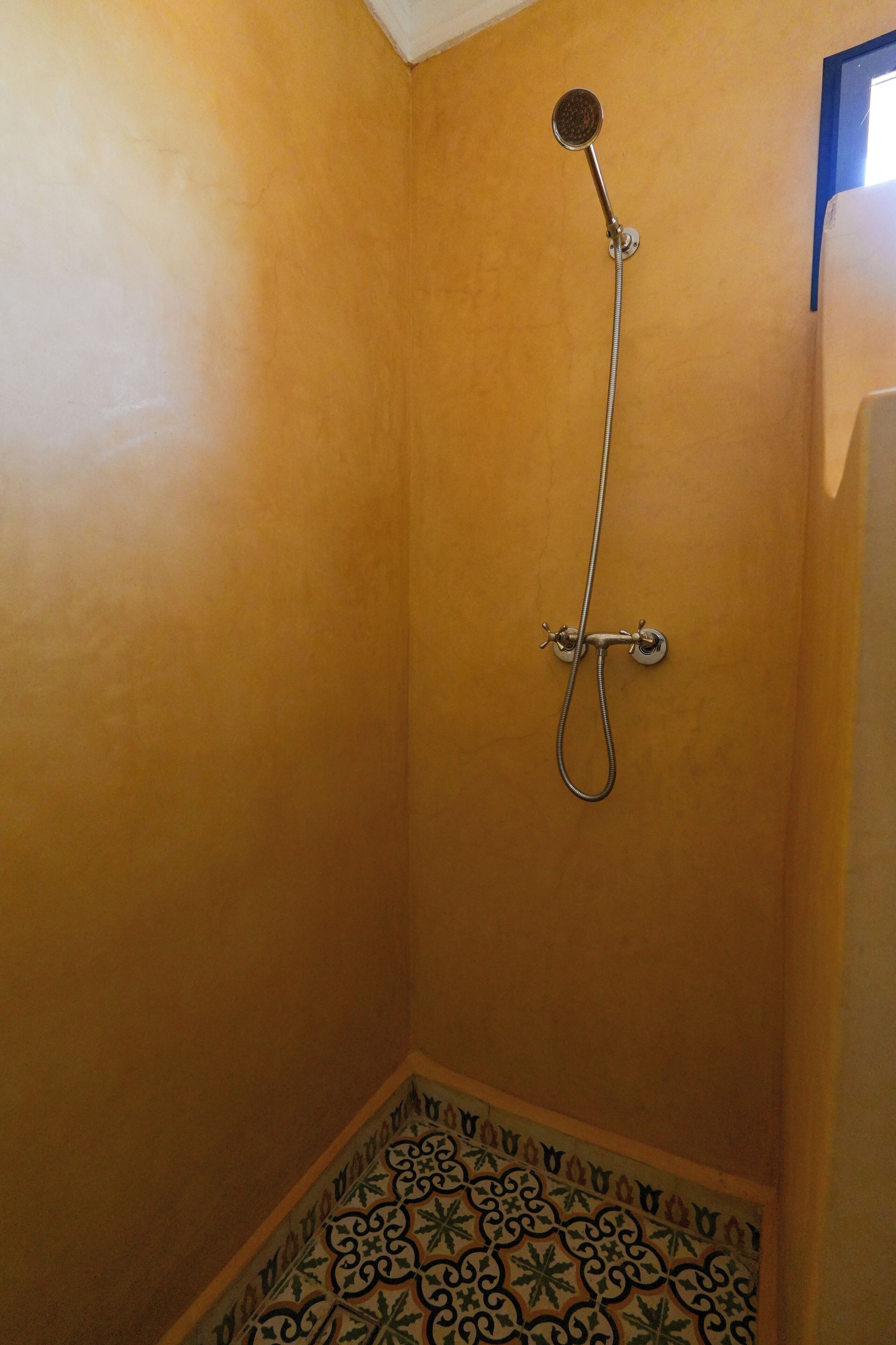 Une salle de bain avec douche, carrelage au sol et agencement d’angle.