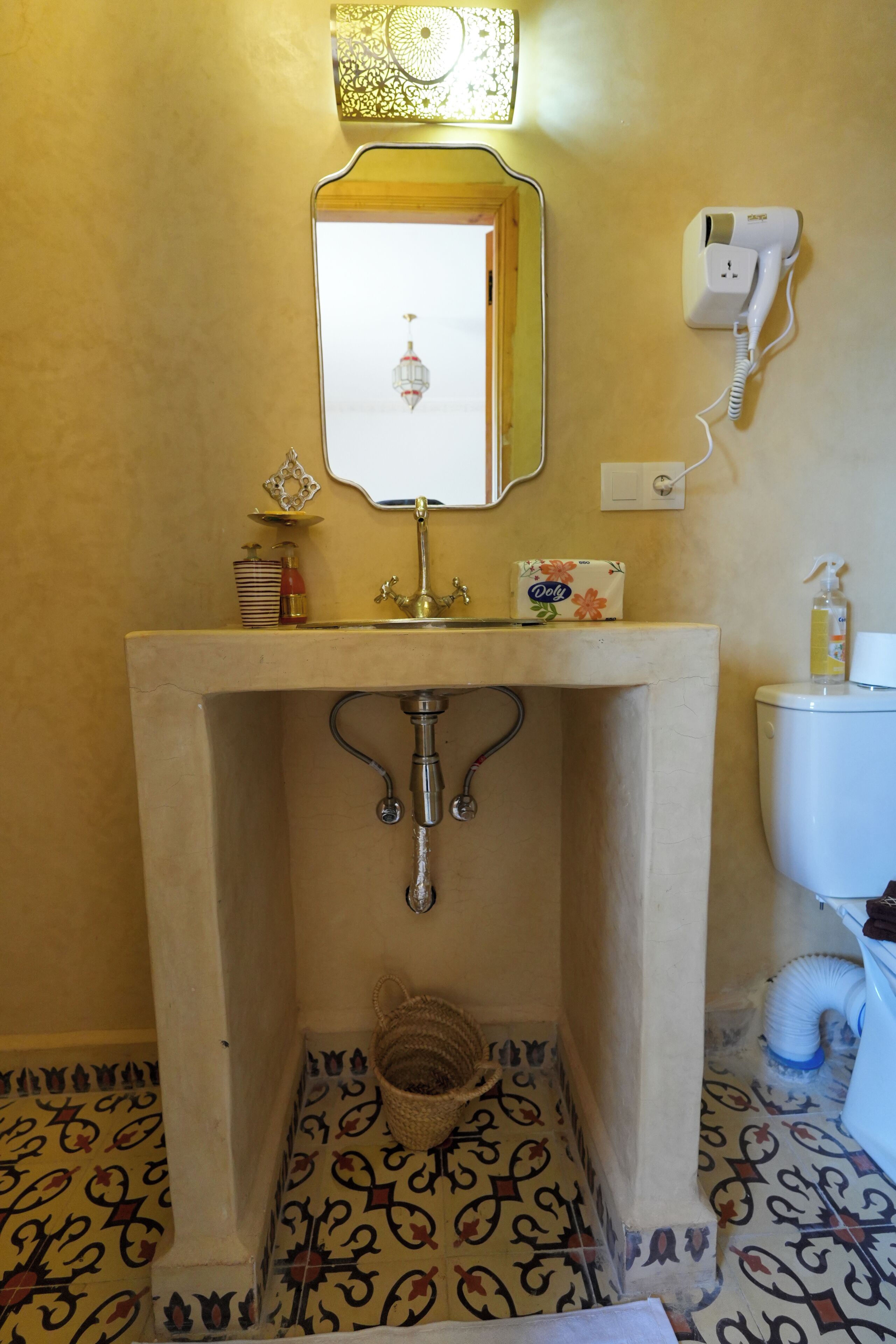 A bathroom with a pedestal sink, a toilet, a hand dryer, and a decorative mirror.