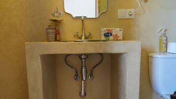 A bathroom with a pedestal sink, a toilet, a hand dryer, and a decorative mirror.