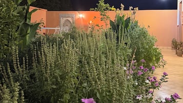 A garden with various plants and flowers, a wall with a decorative pattern, and a building with a light fixture.