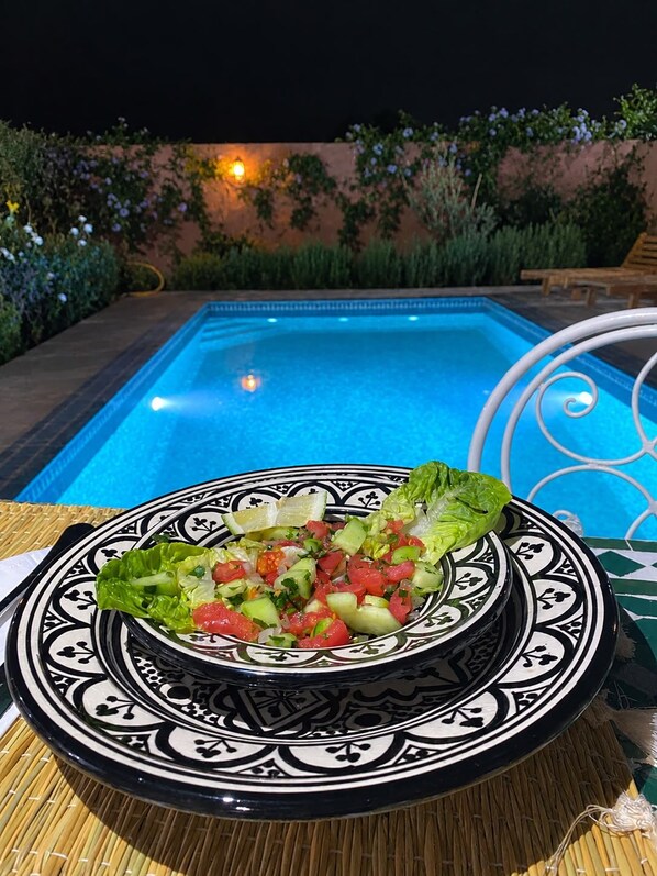 A poolside setting with a table featuring a decorative plate with a salad.