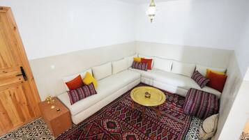 Een zithoek met een witte bank, decoratieve kussens, een ronde salontafel en een vloerkleed met dessin.
