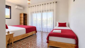 A hotel room with two beds, a wooden wardrobe, a small table, and a patterned floor.