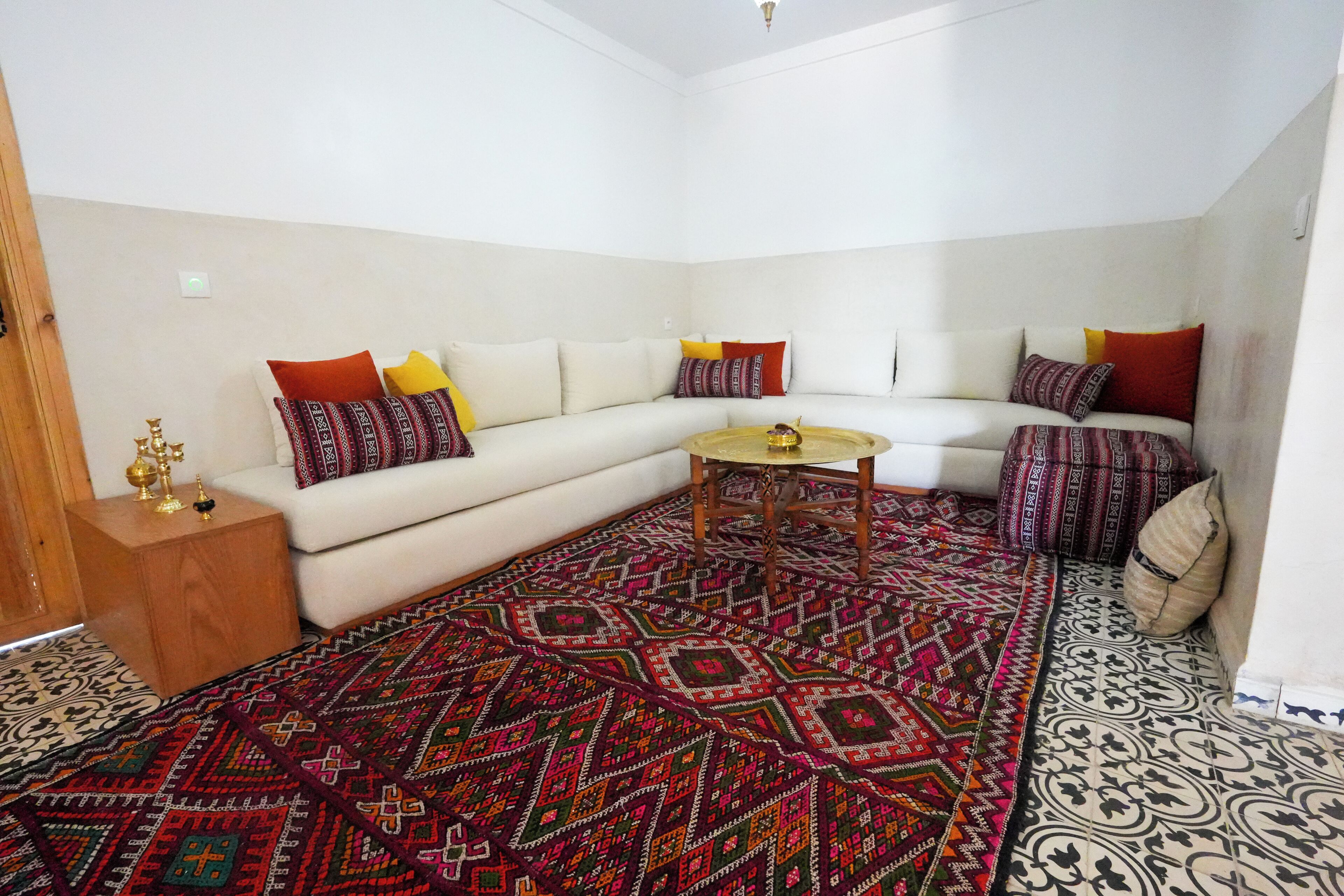 Una sala de estar con un sofá blanco, cojines coloridos, un tapete estampado y una mesita de madera.
