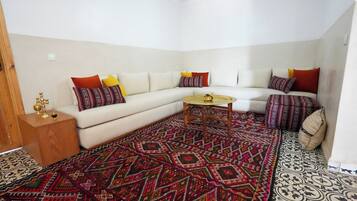 Una sala de estar con un sofá blanco, cojines coloridos, un tapete estampado y una mesita de madera.