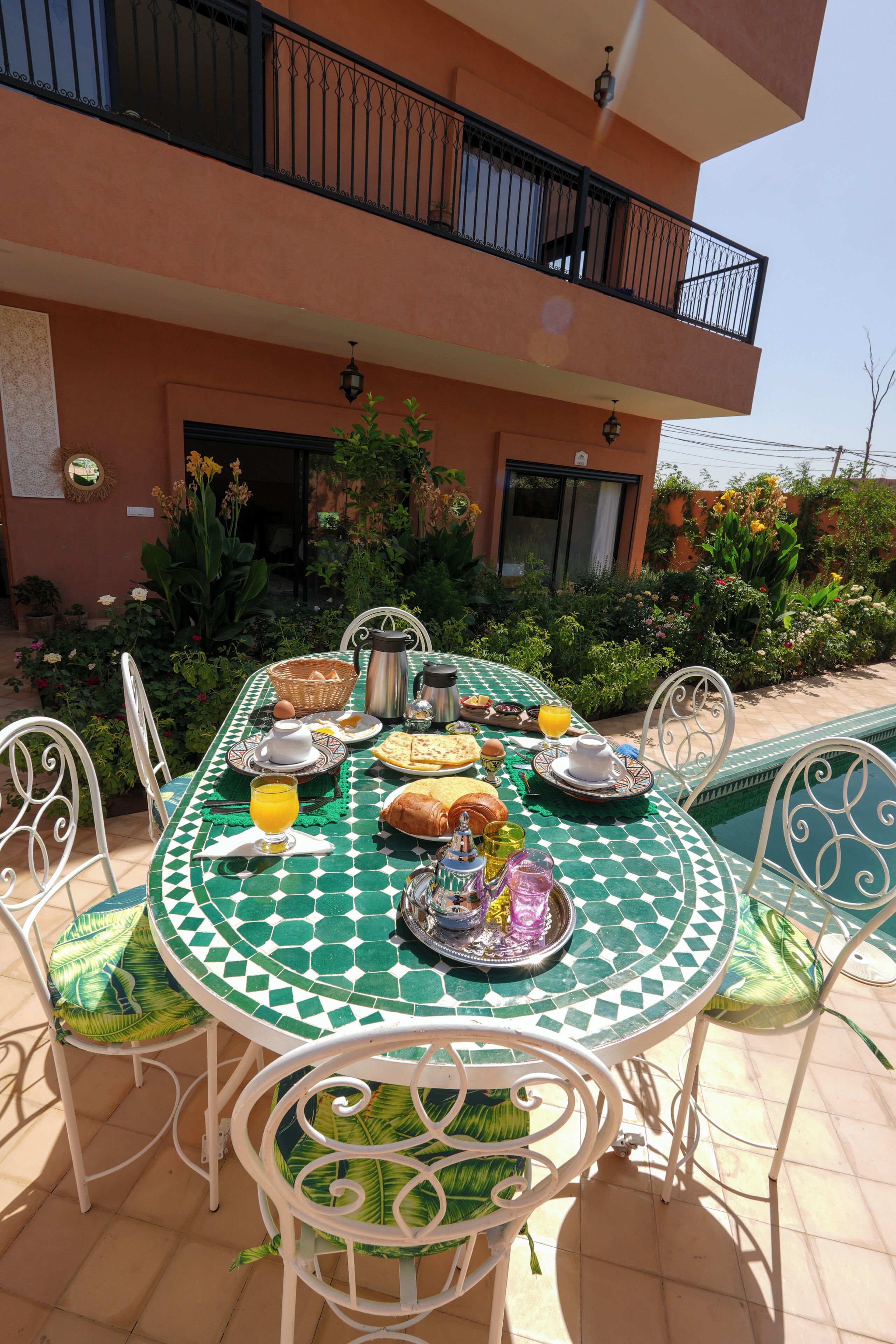 Un área de comedor al aire libre con una mesa dispuesta para el desayuno, rodeada de sillas y con vista a una piscina.