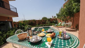 Mesa de comedor con alimentos para el desayuno, piscina y mobiliario exterior.