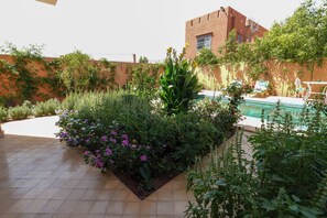 Ein Poolbereich mit gefliestem Deck, umgeben von üppiger Vegetation und blühenden Pflanzen.