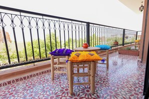 A balcony with a patterned floor, a wooden table, and two chairs with colorful cushions. - Atlas Peak Blue (Sidi Abdallah Ghiat)