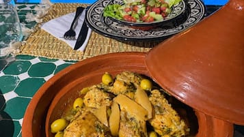 Un tavolo da pranzo con un pasto, una ciotola di stufato e una piscina sullo sfondo.