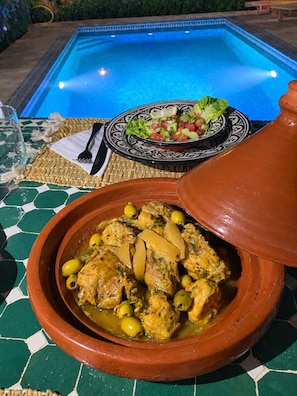 A dining table with a meal, a bowl of stew, and a pool in the background.