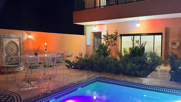 Zona de piscina al aire libre con mobiliario de comedor y un balcón.