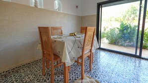 Un comedor con una mesa dispuesta para cuatro, sillas de madera, piso con diseño y vista a la vegetación a través de un ventanal.