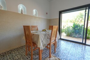 A dining area with a table set for four, wooden chairs, a patterned floor, and a view of greenery through a glass door. - Atlas Peak Blue (Sidi Abdallah Ghiat)