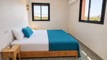 A bedroom with a bed, a nightstand, a window, and patterned flooring.