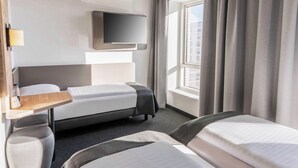 Habitación de hotel con cama, escritorio, televisor y ventana con cortinas.